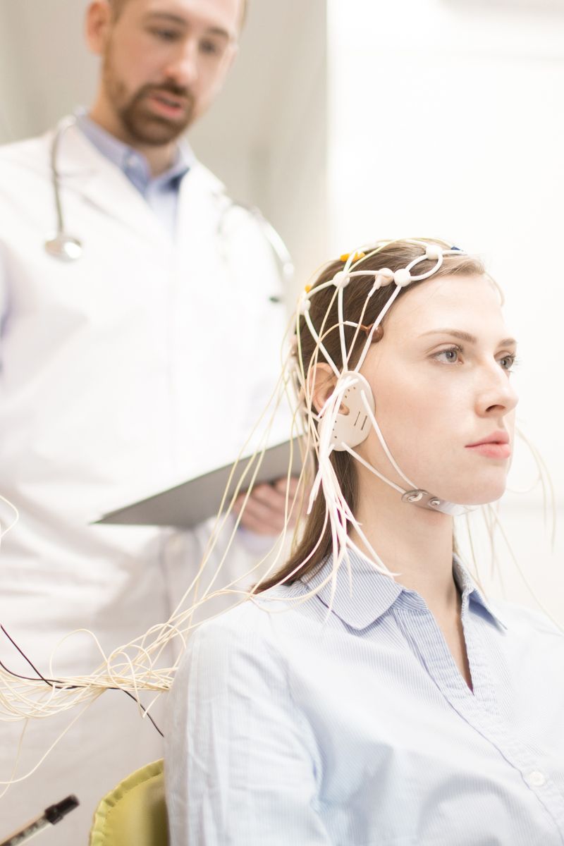 A woman is sitting in a doctor's office undergoing tests with wires attached to her head.