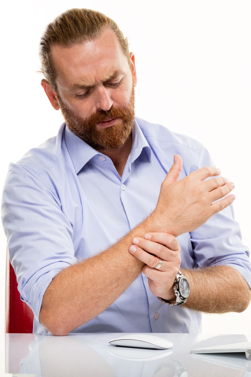 A man with a beard is holding his wrist in pain, seeking assistance from No-Fault and Workers Compensation Doctors.
