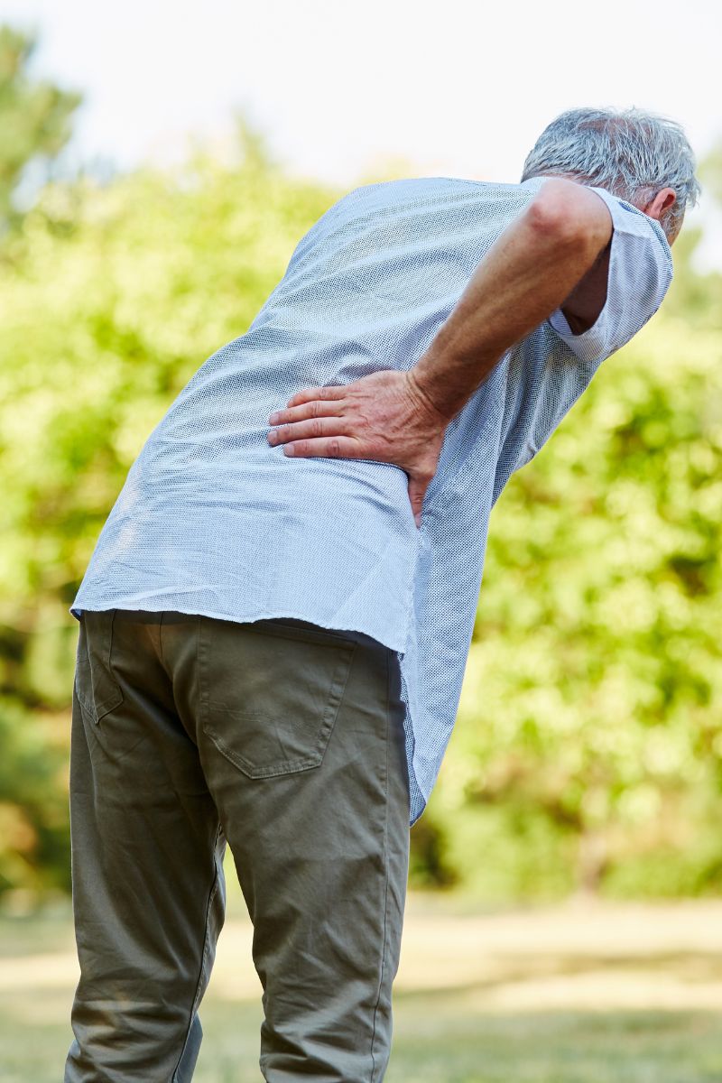 A man with back pain standing in a park seeking No-Fault medical assistance.