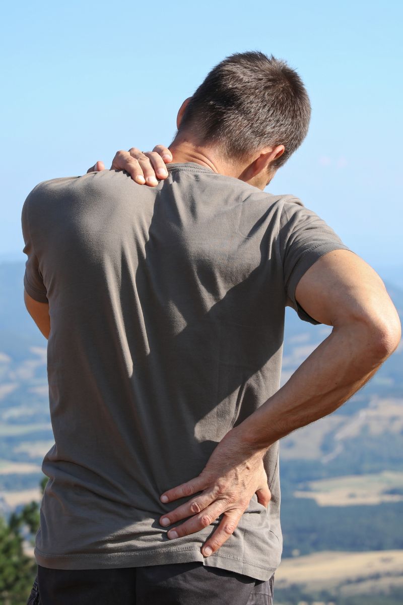 A man with back pain seeking treatment from a Workers Compensation Doctor on top of a mountain.