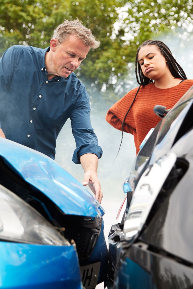 A man and woman standing next to a damaged car in need of workers compensation doctors.