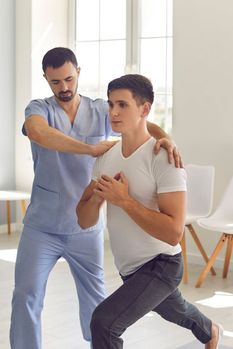 A man is doing exercises with a colleague in a physical therapy room.