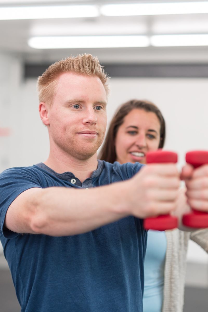 A man and woman exercising with dumbbells in a gym.