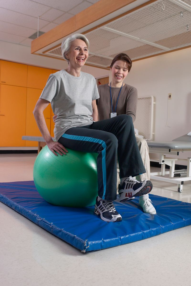 Two women utilizing an exercise ball in a hospital room for their workers compensation therapy.