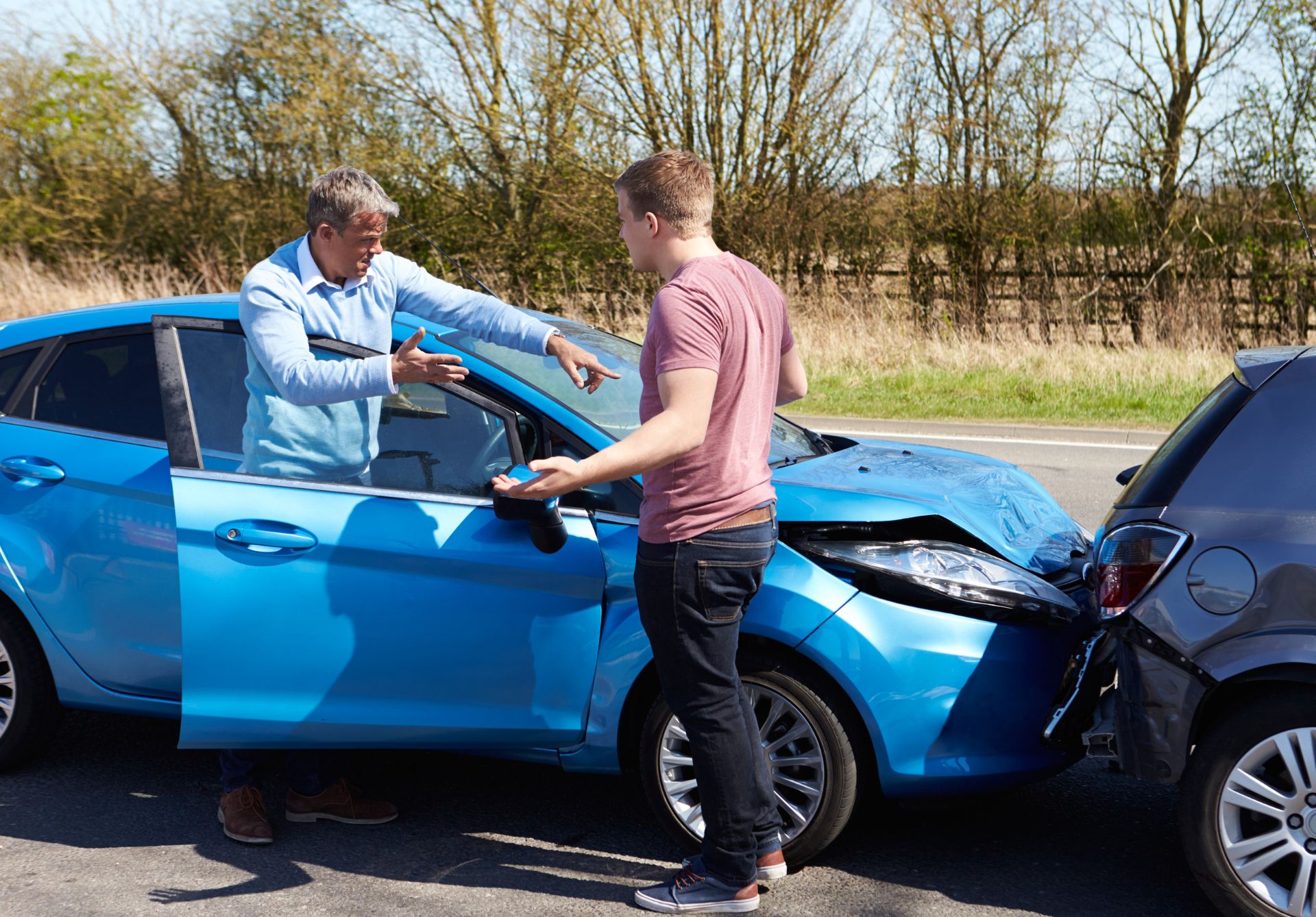 Two men standing next to a blue car after a car accident involving workers compensation.