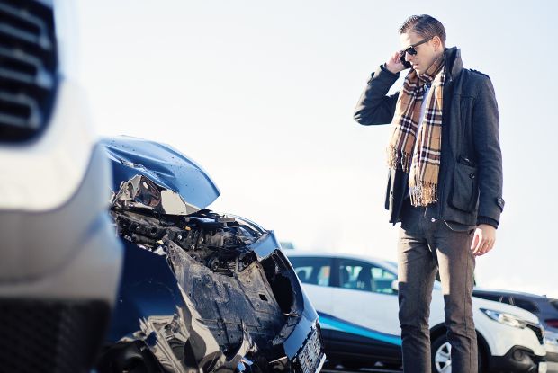 A man standing next to a wrecked car on the side of the road after an accident.
