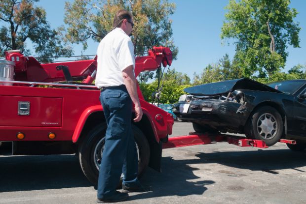 A man is towing a car on a tow truck, with no-fault insurance coverage.