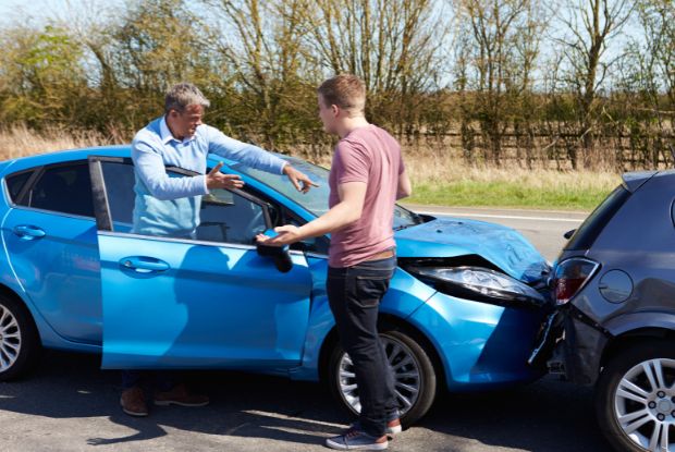 Two men standing next to a blue car after a car accident, seeking assistance from workers compensation doctors.