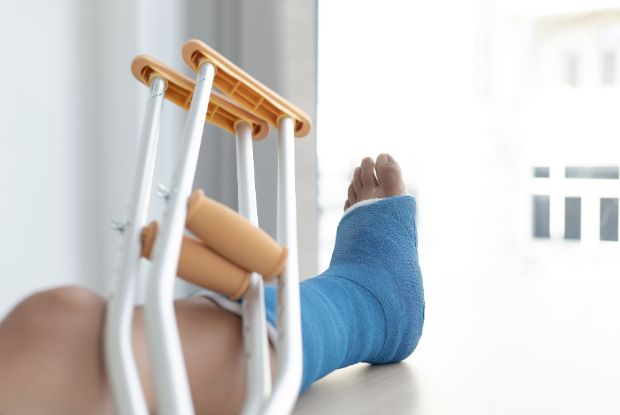 A person's injured leg with a cast and crutches on a table, in need of No-Fault doctors or Workers Compensation doctors.