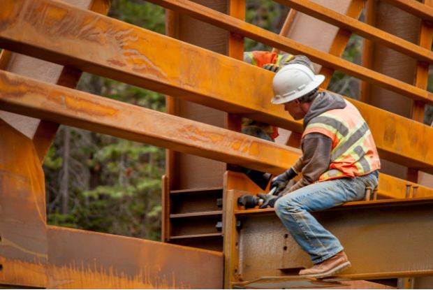 Two construction workers working on a steel bridge, requiring consultation with no-fault and workers compensation doctors.