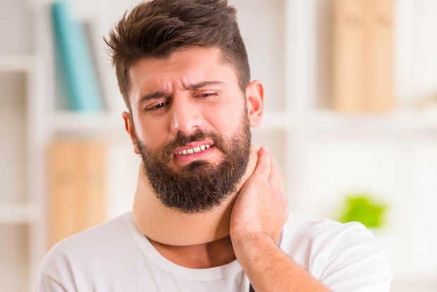 A man with a neck injury is holding his neck and in need of Workers Compensation Doctors.