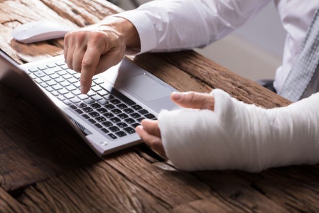 A man with a cast on his arm using a laptop for workers compensation.