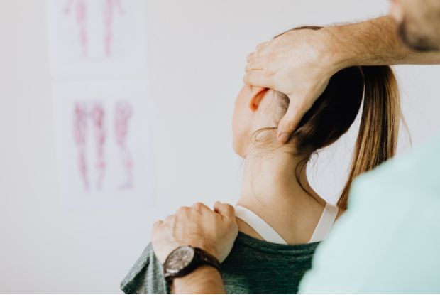 A woman is being examined by a physiotherapist for neck pain, potentially related to a workplace injury.