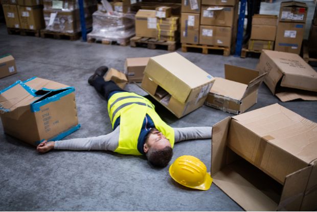 A worker injured and incapacitated on the floor in a warehouse, requiring No-Fault or Workers Compensation Doctors.