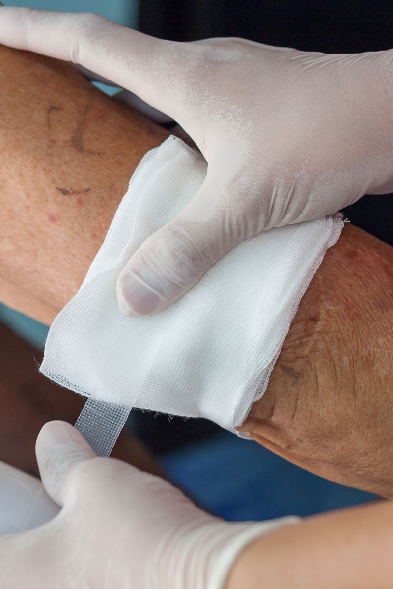 A person is administering wound care by placing a bandage on an elderly person's arm.