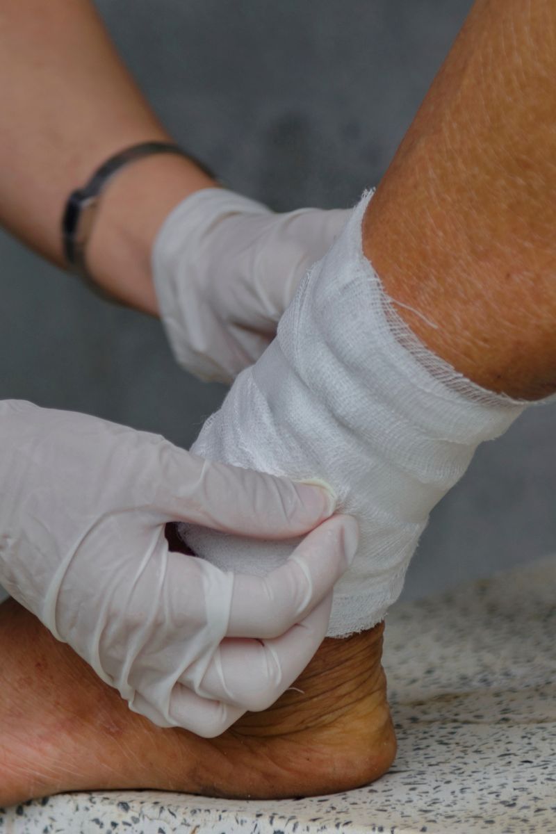 A person providing wound care by putting a bandage on another person's foot.