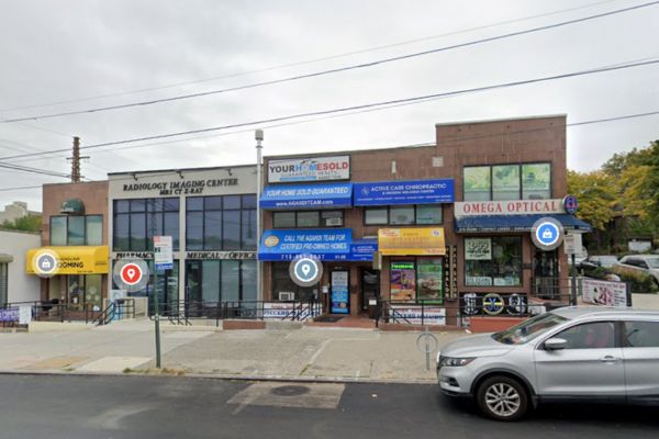 Street view of a bustling row of commercial businesses in Rego Park, NY, featuring a radiology imaging center that specializes in Workers' Compensation claims, a charming thrift store, and an optical shop, with parked cars lining the street.