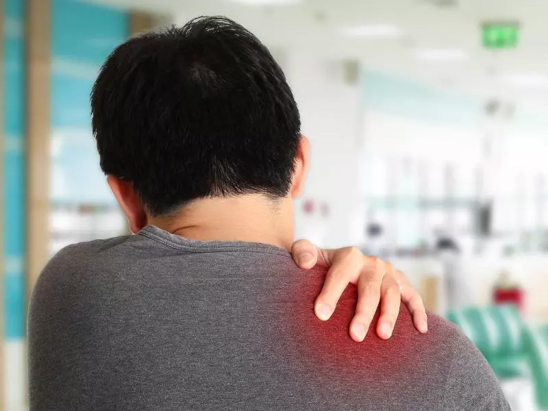 Person holding their shoulder, highlighting discomfort or pain with a red area on the shoulder.