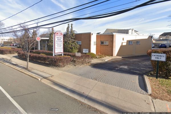 A one-story brick building in Amityville NY with an "Entrance Only" sign by a driveway and a directory sign near a sidewalk, home to No-Fault Doctors and Workers Compensation Doctors on a sunny day.